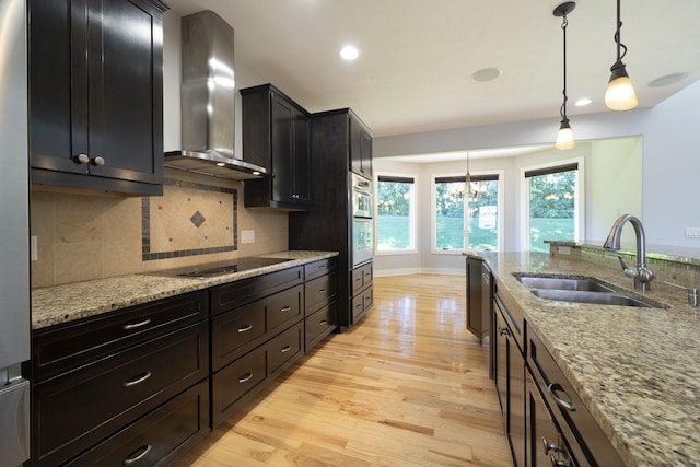 kitchen with light stone countertops, tasteful backsplash, sink, wall chimney range hood, and decorative light fixtures