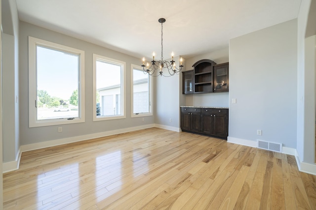 unfurnished dining area with a chandelier and light wood-type flooring