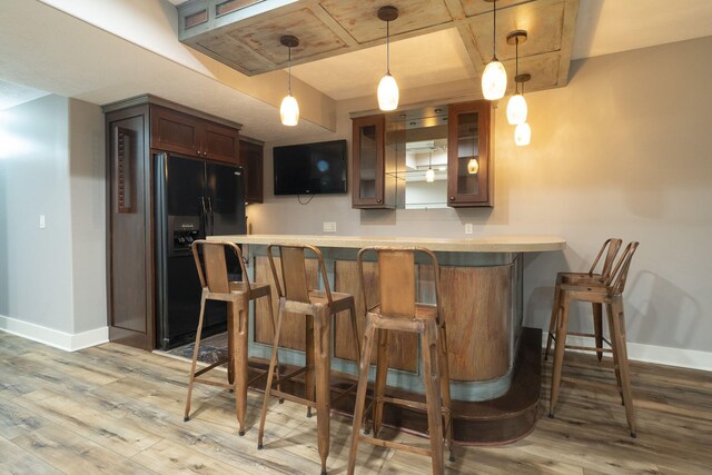 bar featuring black fridge with ice dispenser, light wood-type flooring, and hanging light fixtures