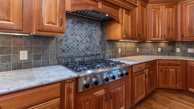 kitchen with backsplash, light hardwood / wood-style floors, light stone countertops, exhaust hood, and stainless steel gas stovetop