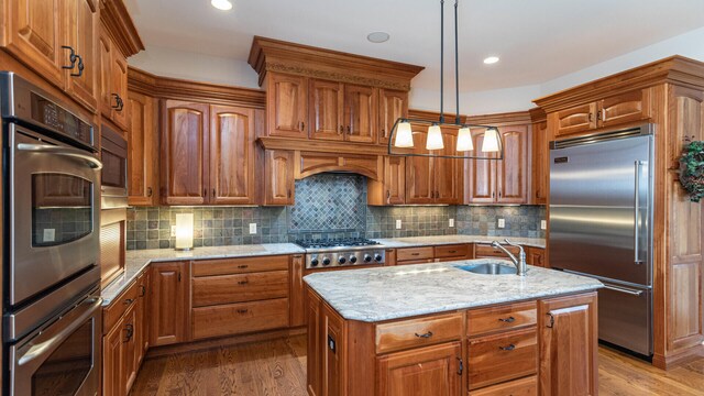 kitchen featuring sink, built in appliances, hanging light fixtures, an island with sink, and hardwood / wood-style floors