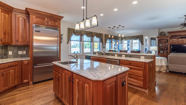 kitchen with sink, tasteful backsplash, decorative light fixtures, appliances with stainless steel finishes, and a kitchen island with sink