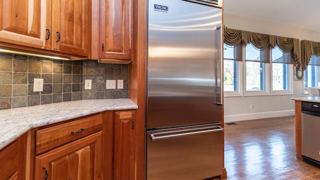 kitchen with light stone counters, backsplash, hardwood / wood-style flooring, and appliances with stainless steel finishes