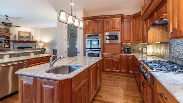 kitchen with appliances with stainless steel finishes, decorative light fixtures, an island with sink, sink, and backsplash