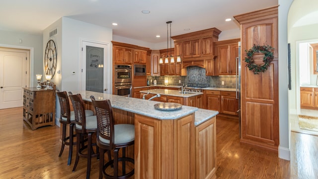 kitchen featuring decorative light fixtures, appliances with stainless steel finishes, dark hardwood / wood-style floors, a kitchen island with sink, and backsplash