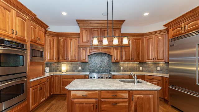 kitchen featuring built in appliances, sink, hanging light fixtures, and an island with sink