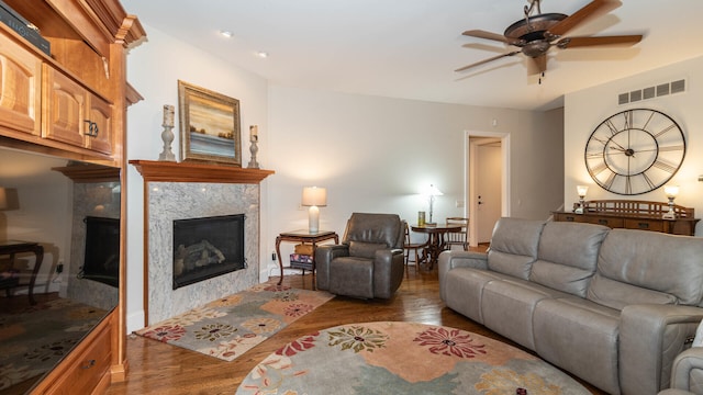 living room featuring ceiling fan, a premium fireplace, and dark hardwood / wood-style flooring