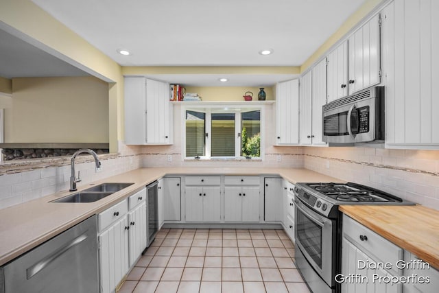 kitchen with sink, light tile patterned floors, backsplash, white cabinets, and appliances with stainless steel finishes