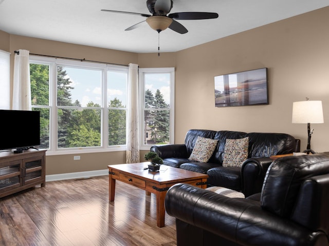 living area with baseboards, plenty of natural light, wood finished floors, and a ceiling fan