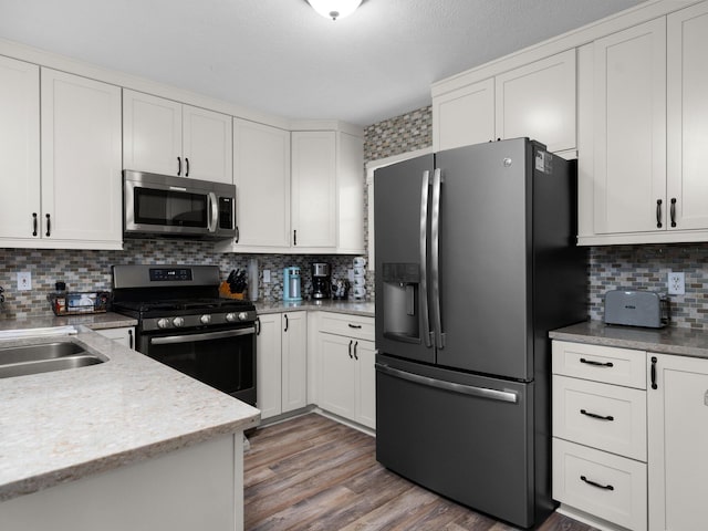 kitchen featuring wood-type flooring, stainless steel appliances, decorative backsplash, and white cabinetry