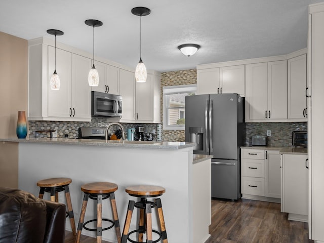 kitchen featuring a peninsula, stainless steel appliances, dark wood-type flooring, white cabinets, and a kitchen breakfast bar