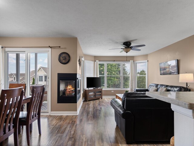 living room featuring a textured ceiling, dark wood-type flooring, ceiling fan, and a multi sided fireplace