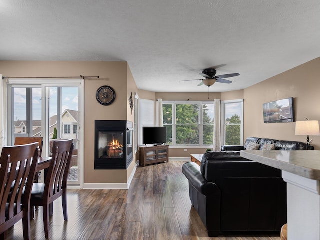 living room with baseboards, a multi sided fireplace, a healthy amount of sunlight, and wood finished floors