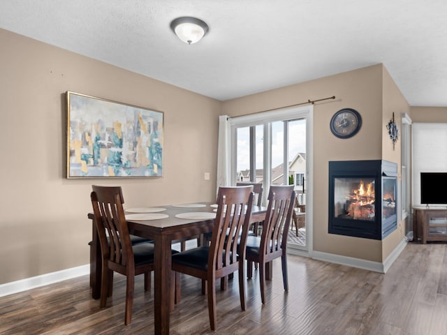 dining room with a textured ceiling, dark wood-type flooring, and a multi sided fireplace