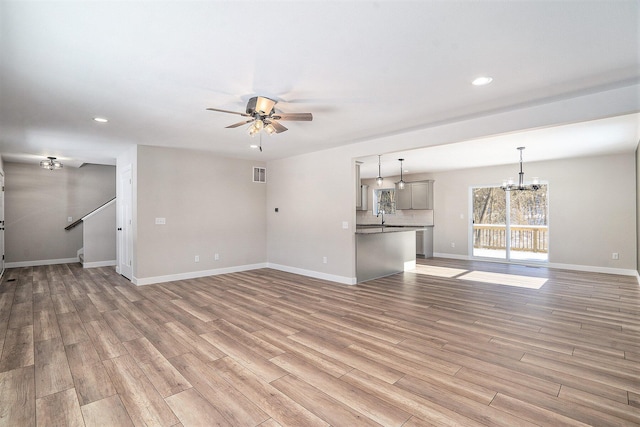 unfurnished living room with ceiling fan with notable chandelier, light wood-type flooring, and sink