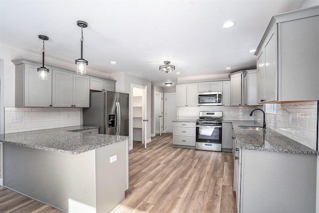 kitchen with pendant lighting, backsplash, sink, appliances with stainless steel finishes, and kitchen peninsula