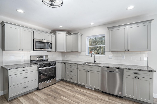 kitchen with light stone countertops, appliances with stainless steel finishes, light hardwood / wood-style floors, and sink