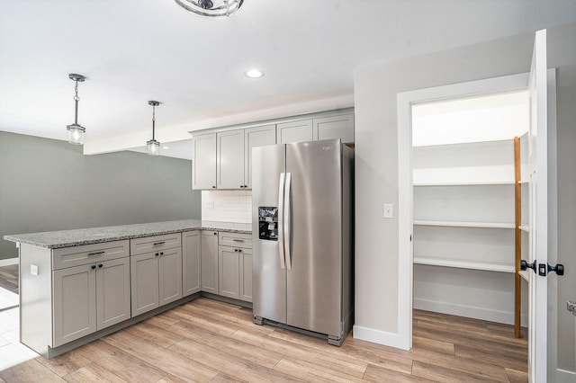 kitchen featuring light stone countertops, stainless steel refrigerator with ice dispenser, light wood-type flooring, decorative backsplash, and pendant lighting