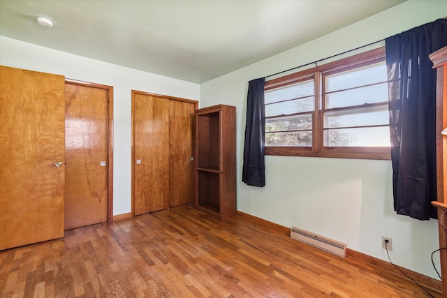 unfurnished bedroom featuring a baseboard heating unit, wood-type flooring, and multiple closets