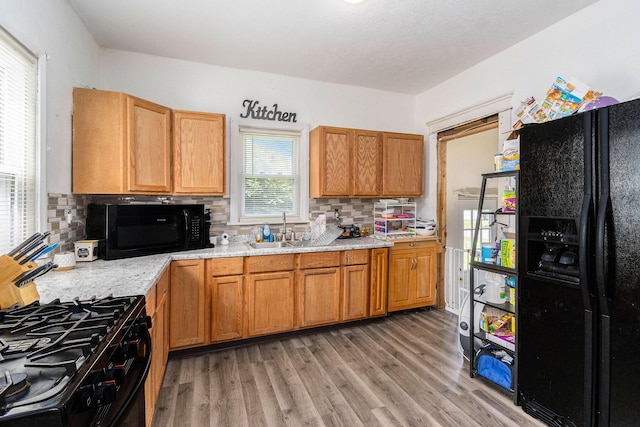 kitchen with decorative backsplash, light wood-style floors, brown cabinetry, black appliances, and a sink