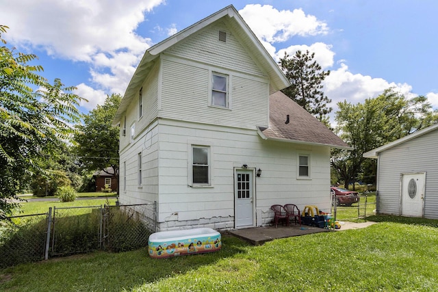 back of house with roof with shingles, a lawn, and fence