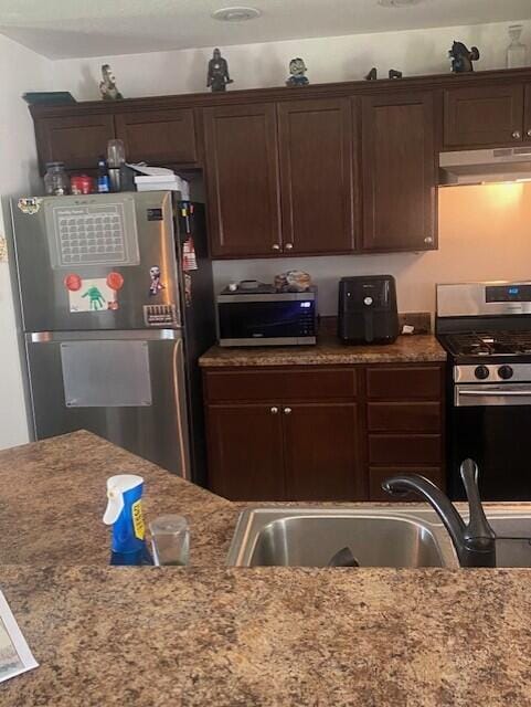 kitchen with sink, light stone countertops, stainless steel appliances, and dark brown cabinetry