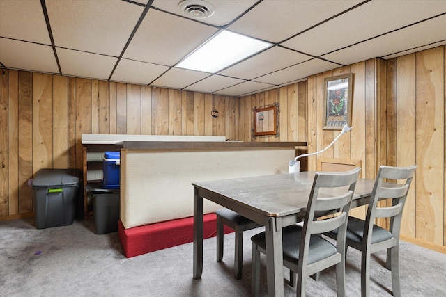 dining space featuring a paneled ceiling, wooden walls, and carpet floors