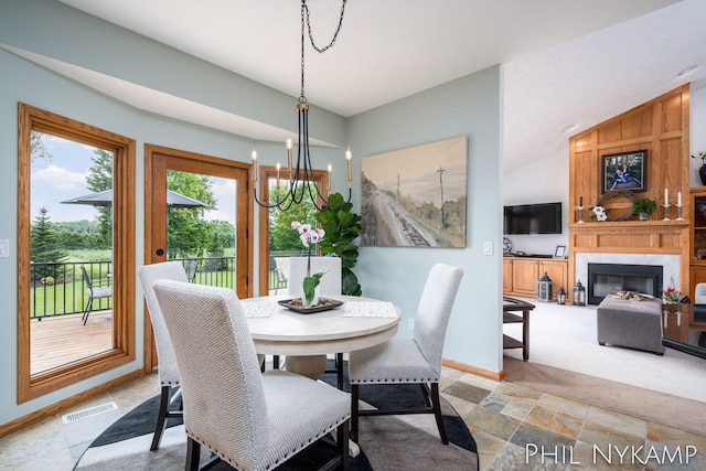 dining area with lofted ceiling, a large fireplace, light colored carpet, and a notable chandelier