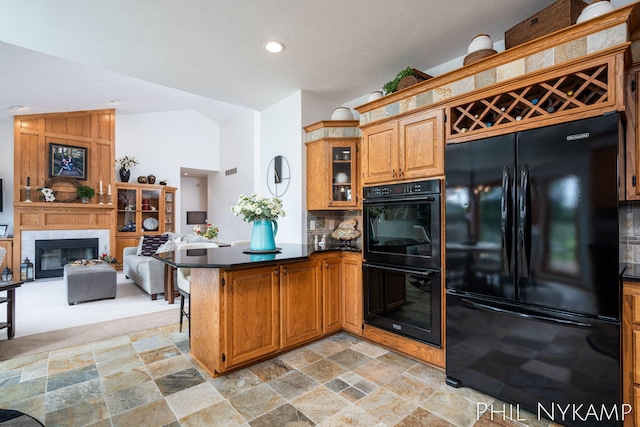 kitchen featuring vaulted ceiling, a large fireplace, kitchen peninsula, and black appliances