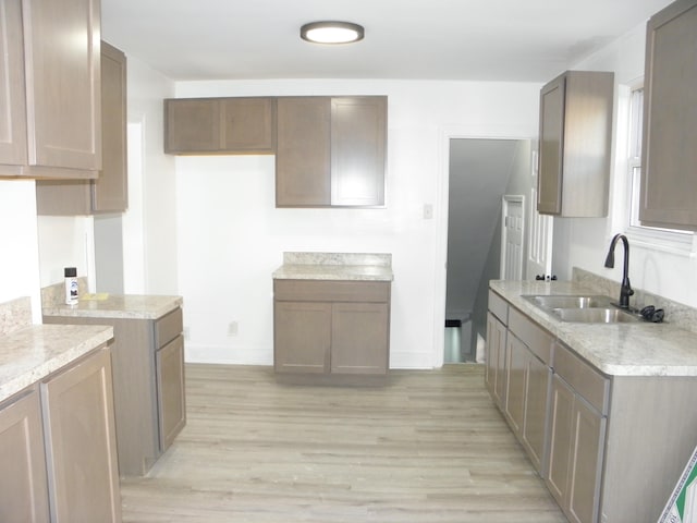 kitchen with sink, light stone counters, and light wood-type flooring