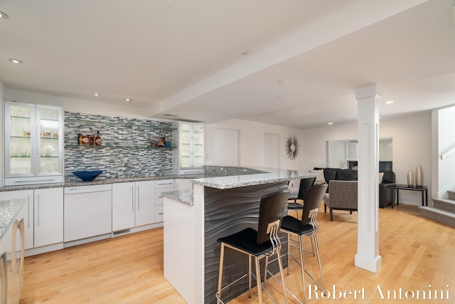 kitchen featuring light wood-type flooring, backsplash, light stone countertops, and white cabinetry