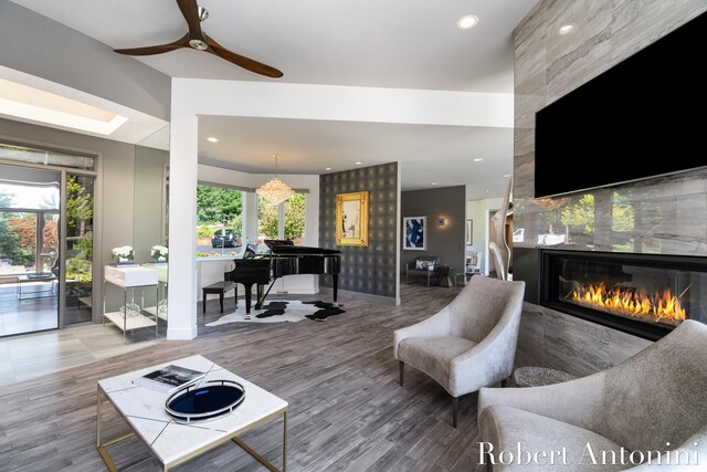 living room with ceiling fan, a tiled fireplace, and wood-type flooring