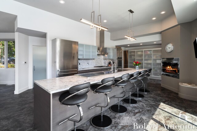 kitchen with pendant lighting, stainless steel appliances, a kitchen breakfast bar, light stone countertops, and wall chimney exhaust hood