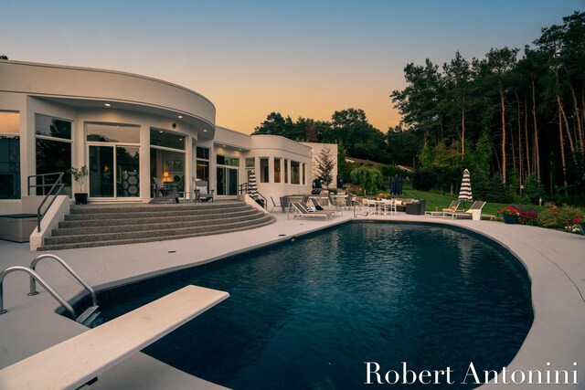 pool at dusk featuring a diving board and a patio