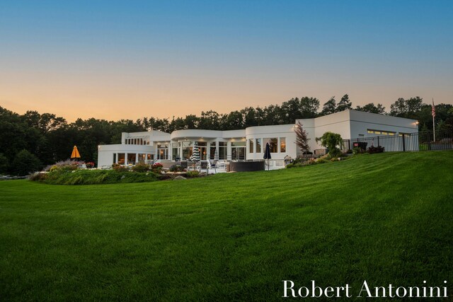 back house at dusk featuring a lawn