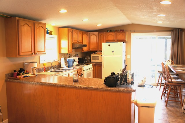 kitchen featuring white appliances, sink, vaulted ceiling, a textured ceiling, and kitchen peninsula