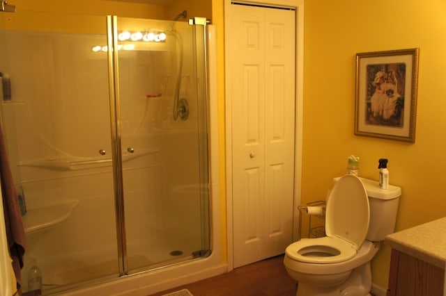 bathroom featuring wood-type flooring, vanity, a shower with shower door, and toilet