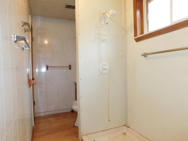 bathroom with hardwood / wood-style flooring, tiled shower, and toilet