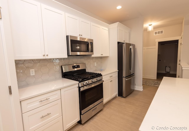 kitchen with tasteful backsplash, white cabinetry, stainless steel appliances, and light hardwood / wood-style floors