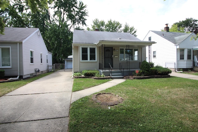 bungalow featuring a porch, a garage, a front lawn, and an outbuilding