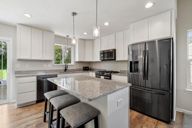 kitchen featuring sink, white cabinetry, a center island, hanging light fixtures, and appliances with stainless steel finishes