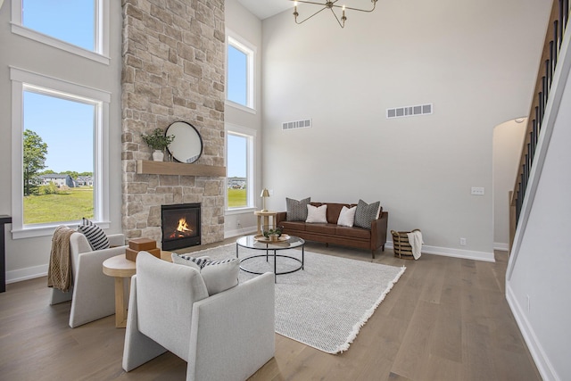 living room with an inviting chandelier, wood-type flooring, a stone fireplace, and a high ceiling