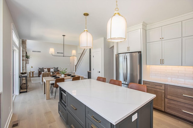 kitchen featuring a kitchen island, stainless steel refrigerator, decorative light fixtures, white cabinetry, and light hardwood / wood-style floors