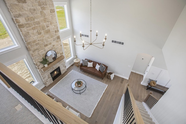 living room with hardwood / wood-style floors, a towering ceiling, a stone fireplace, and a notable chandelier