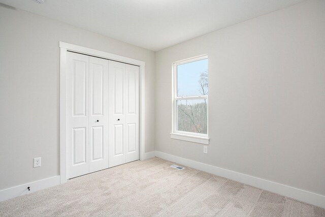 unfurnished bedroom with a closet and light colored carpet