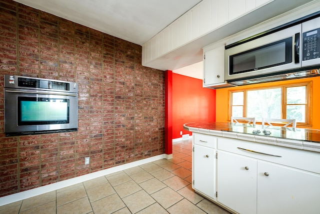 kitchen with tile countertops, white cabinetry, brick wall, and appliances with stainless steel finishes