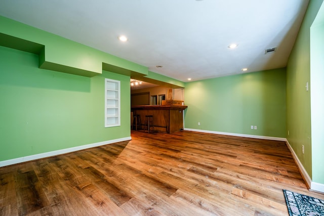 unfurnished living room with bar, built in features, and wood-type flooring