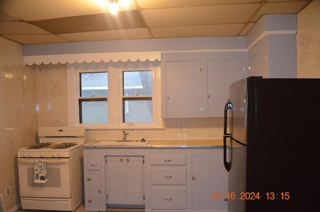 kitchen with black refrigerator, white cabinetry, sink, white range with gas cooktop, and a drop ceiling