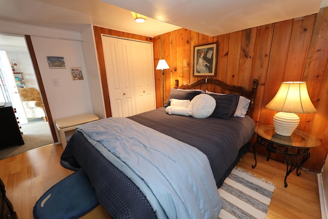 bedroom with light hardwood / wood-style flooring, wood walls, and a closet