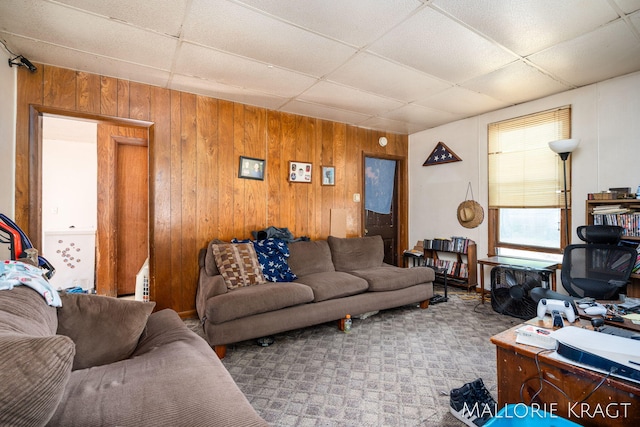 living room featuring wood walls, a drop ceiling, and light colored carpet